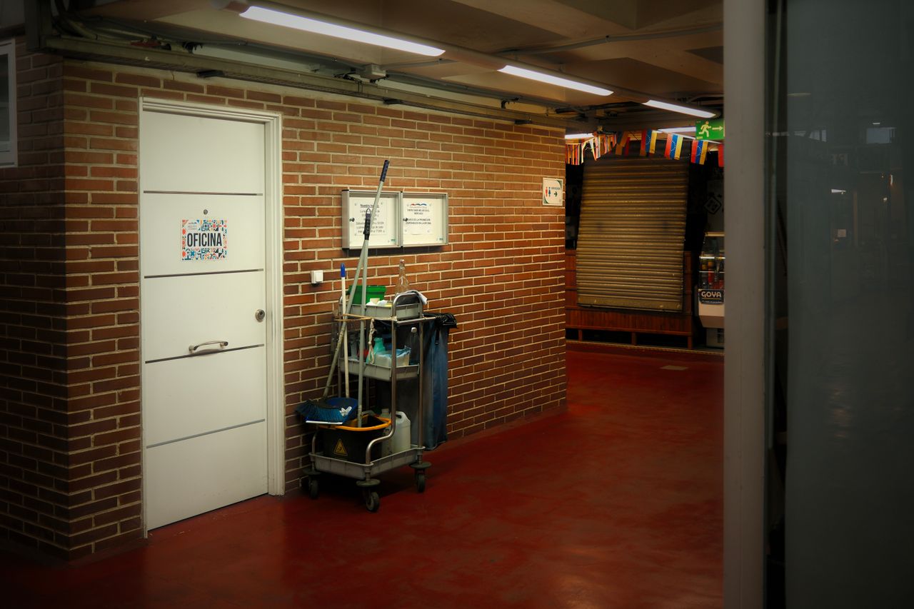 team-01 A brightly lit industrial hallway with a cleaning cart and supplies near an office door.
